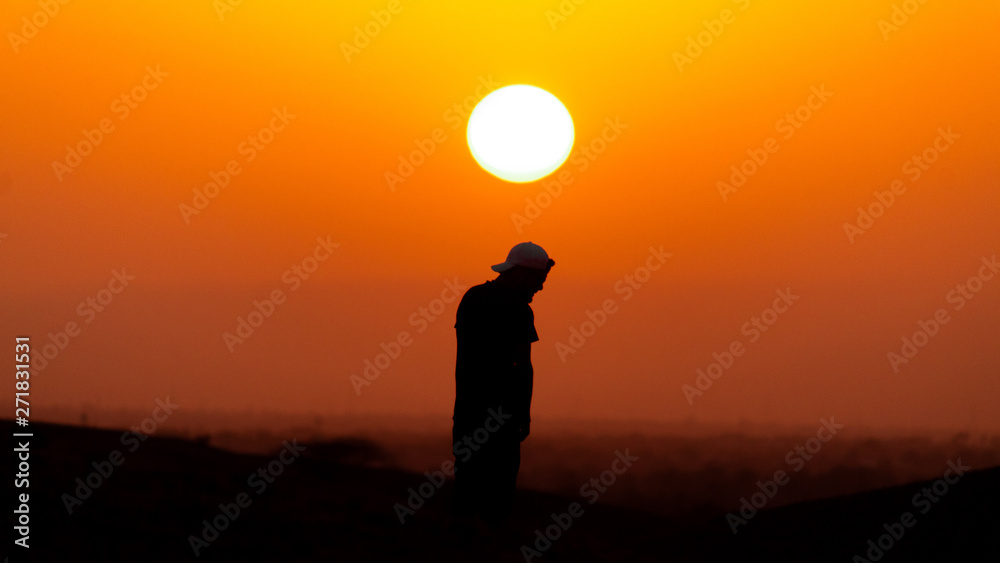 Silhouette of a man standing at the top of the mountain and standing below the sun during sunset