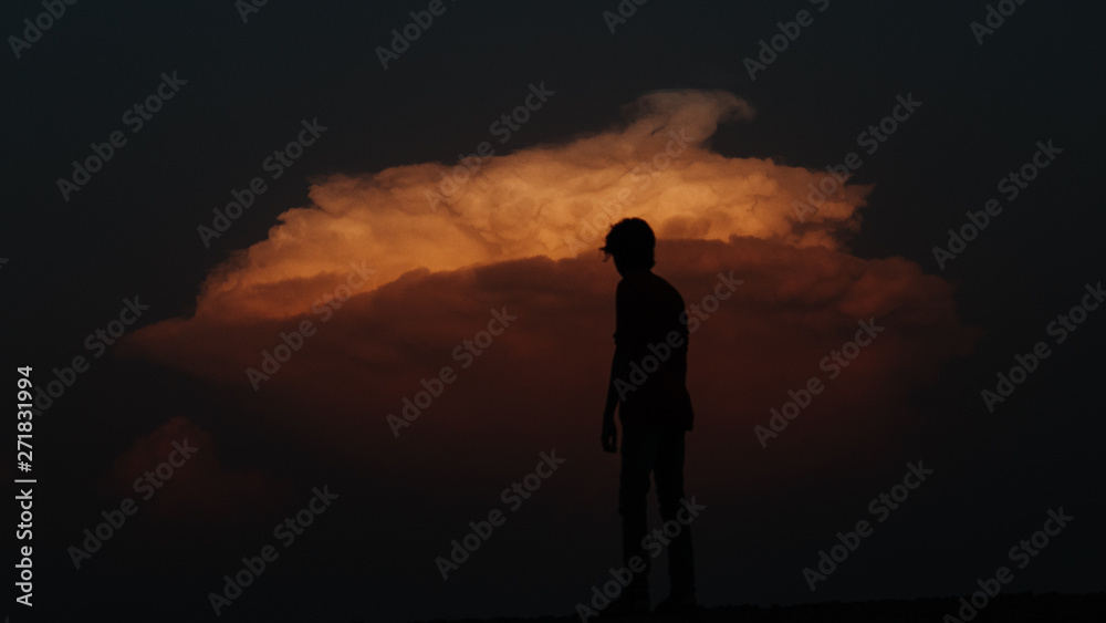Silhouette of man standing in front of dramatic orange sky during sunset