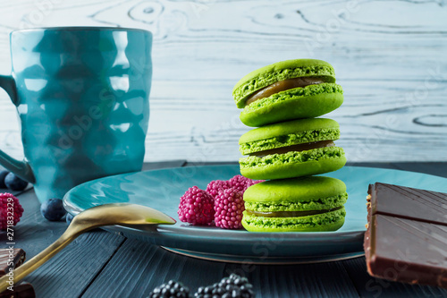 THREE FRENCH CAKES MACARONS GREEN ON A PLATE WITH BERRY MARMELADE WITH COFFEE СUP ON WOODEN WHITE AND GRAY BACKGROUND photo