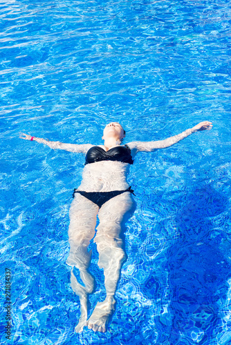 woman with black swimsuit swimming on a blue water pool, tropical vacation holiday concept