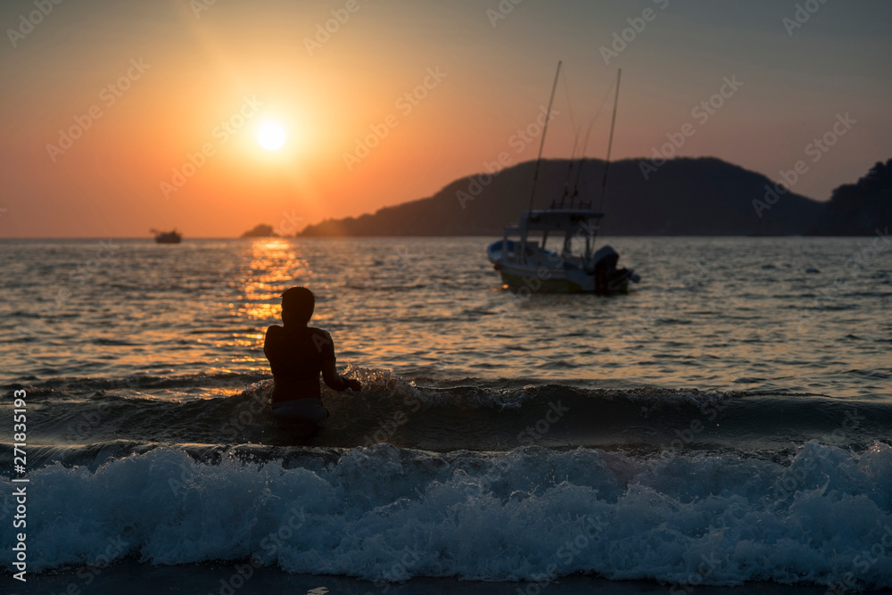 Silhouette of fisherman boy at sunset on the beach and boat background