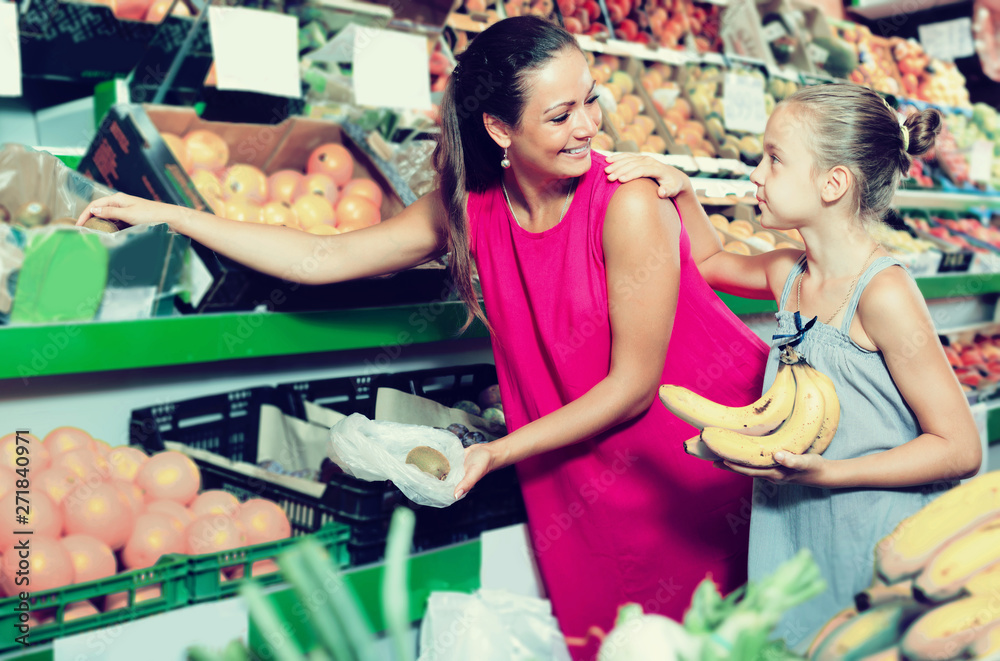 Happy young woman with girl buying various fruits