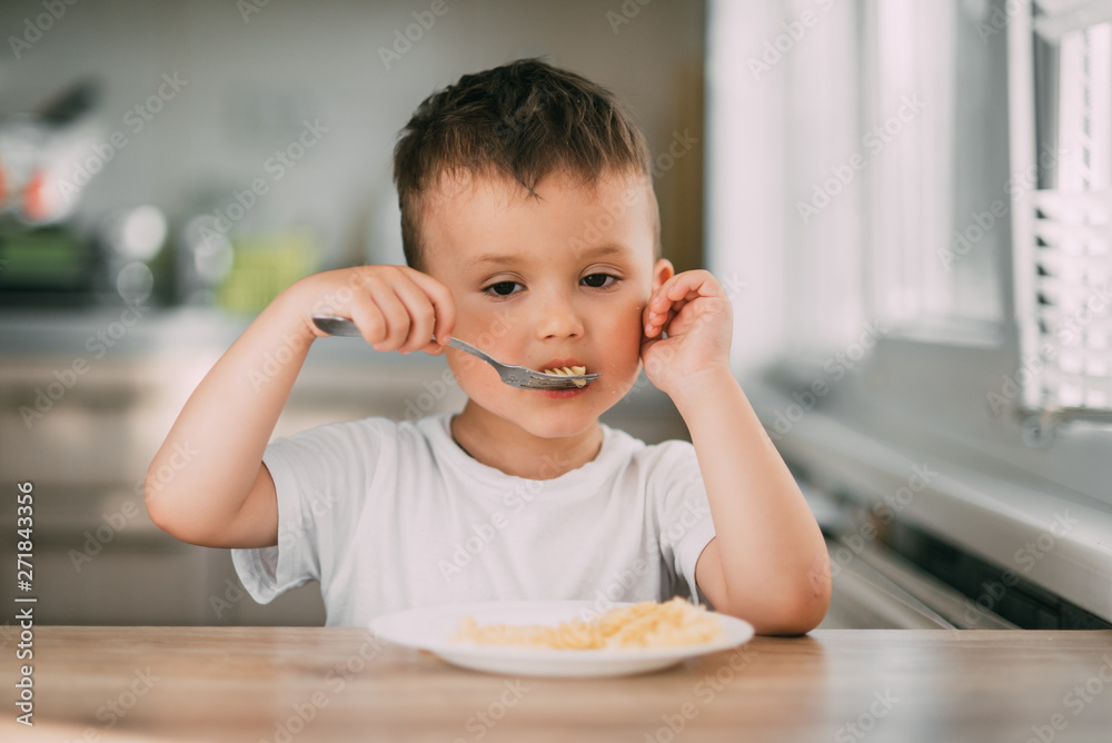 a child in the kitchen during the day eating pasta in a spiral in a white t-shirt a child in the kitchen during the day eating pasta in a spiral in a white t-shirt