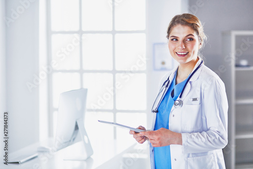 Young woman doctor is standing with board with clipboard smilin