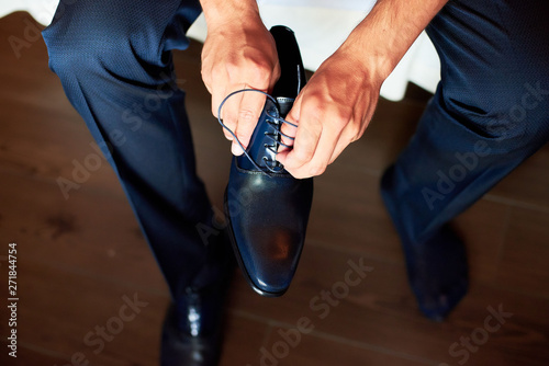 An elegant man puts on black, leather, formal shoes. Tying shoes.