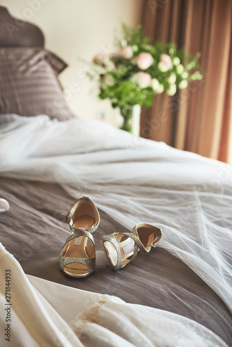 White elegant wedding dress, veil and shoes lying on the bed.