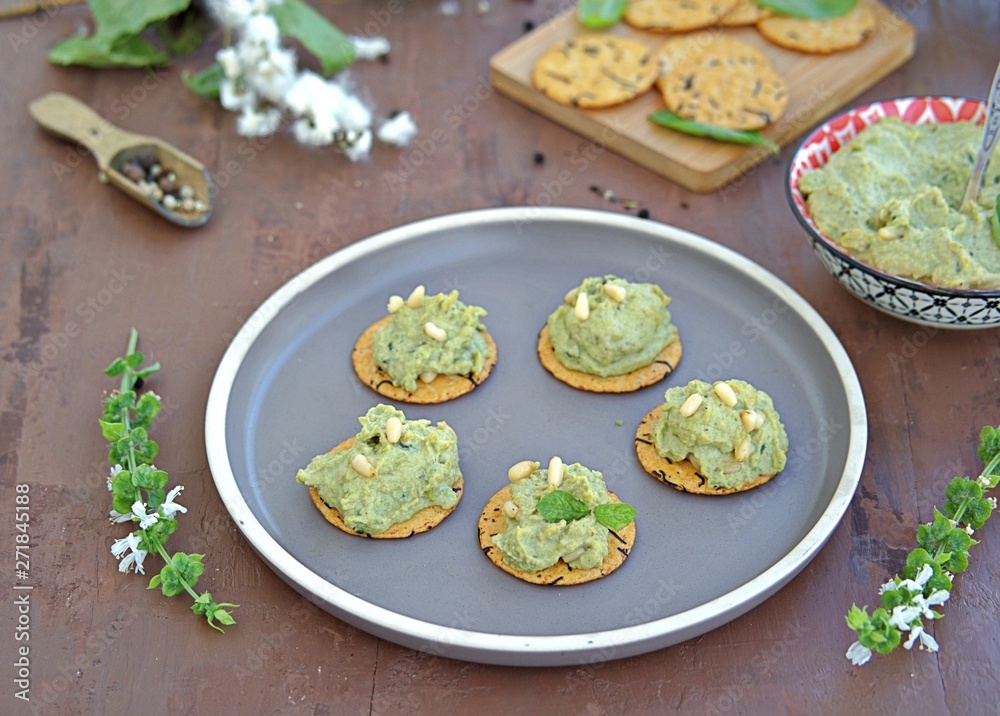 Snack, green pea spread with almonds and basil on unsweetened crackers on a brown clay plate. Healthy snacks. Snack, green pea spread with almonds and basil on unsweetened crackers on a brown clay plate. Healthy snacks.