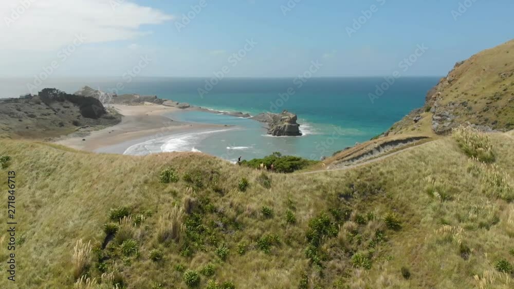 A drone shot orbiting around two people running along the ridgeline of a grassy hilltop with gorgeous teal blue ocean water in the background A drone shot orbiting around two people running along the ridgeline of a grassy hilltop with gorgeous teal blue ocean water in the background