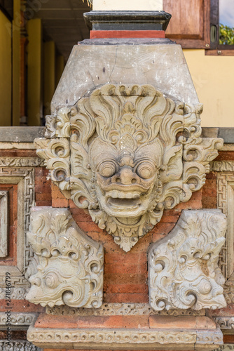 Klungkung, Bali, Indonesia - February 26, 2019: Royal Palace. Closeup of beige mask mural set on red bricks under pillar at entrance museum. photo