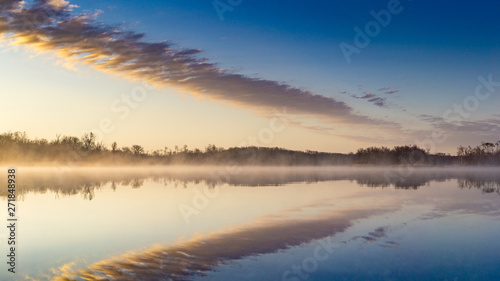 Fototapeta Naklejka Na Ścianę i Meble -  Sunrise lake and sky mirrored images, Calm as glass lake water reflecting the sky above, misty water