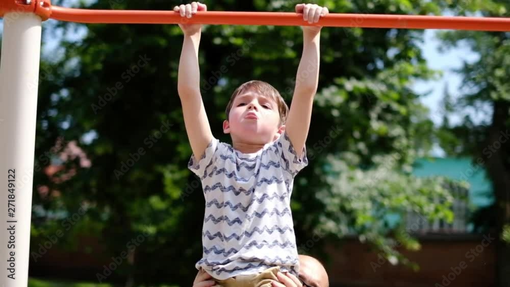 a man in light clothes teaches a boy to climb the horizontal bar correctly in a sunny summer park. Father helps his little son in sports a man in light clothes teaches a boy to climb the horizontal bar correctly in a sunny summer park. Father helps his little son in sports