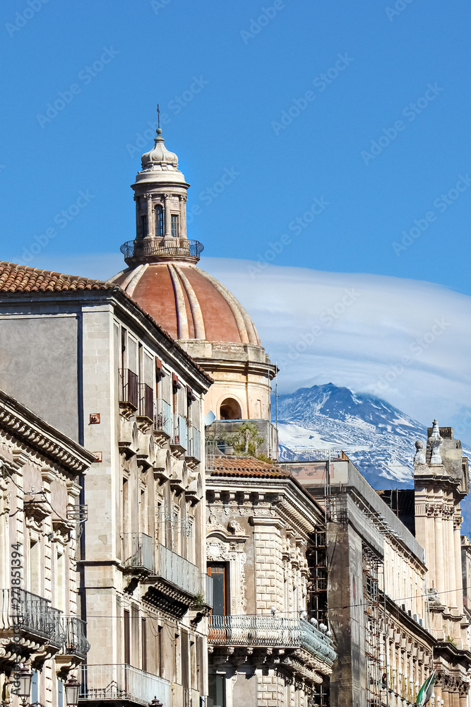 Beautiful close up photography of Catania Cathedral of Saint Agatha with adjacent historical buildings and Mount Etna in the background. Snow on the very top of the famous volcano