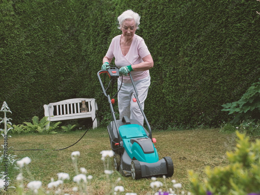 Senior woman mowing the lawn in the garden Senior woman mowing the lawn in the garden