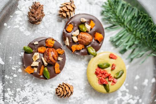 Christmas theme. Handmade chocolates candy. Mini chocolate dessert covered with nuts and dried fruits. Garland lamps bokeh on background. Copy space