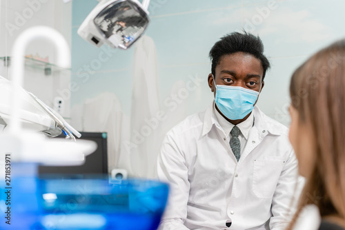 Young African American male doctor dentist in a medical mask. Beautiful girl patient at chair at dental clinic. Medicine  health  stomatology concept. dentist conducts inspection and concludes