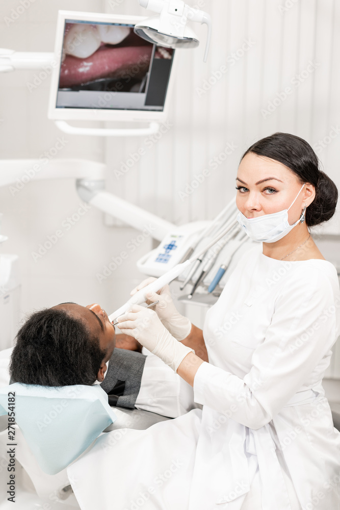 Inspection with a dental macro camera and displays the result on the monitor. Young woman dentist treating root canals in the dental clinic. Man patient lying on dentist chair with open mouth. Inspection with a dental macro camera and displays the result on the monitor. Young woman dentist treating root canals in the dental clinic. Man patient lying on dentist chair with open mouth.