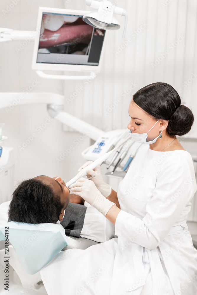 Obraz premium Inspection with a dental macro camera and displays the result on the monitor. Young woman dentist treating root canals in the dental clinic. Man patient lying on dentist chair with open mouth.