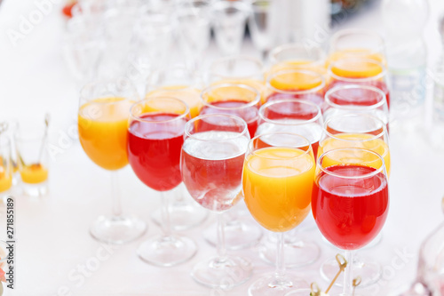 Table top full of glasses Glasses not alcoholic drinks, orange juice, water and berry juice. s with canapes and antipasti in the background. photo