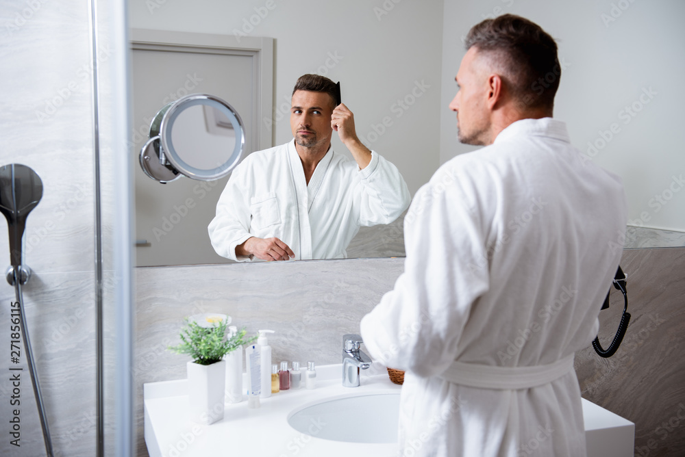 Fototapeta premium Handsome young man combing his hair in front of the mirror