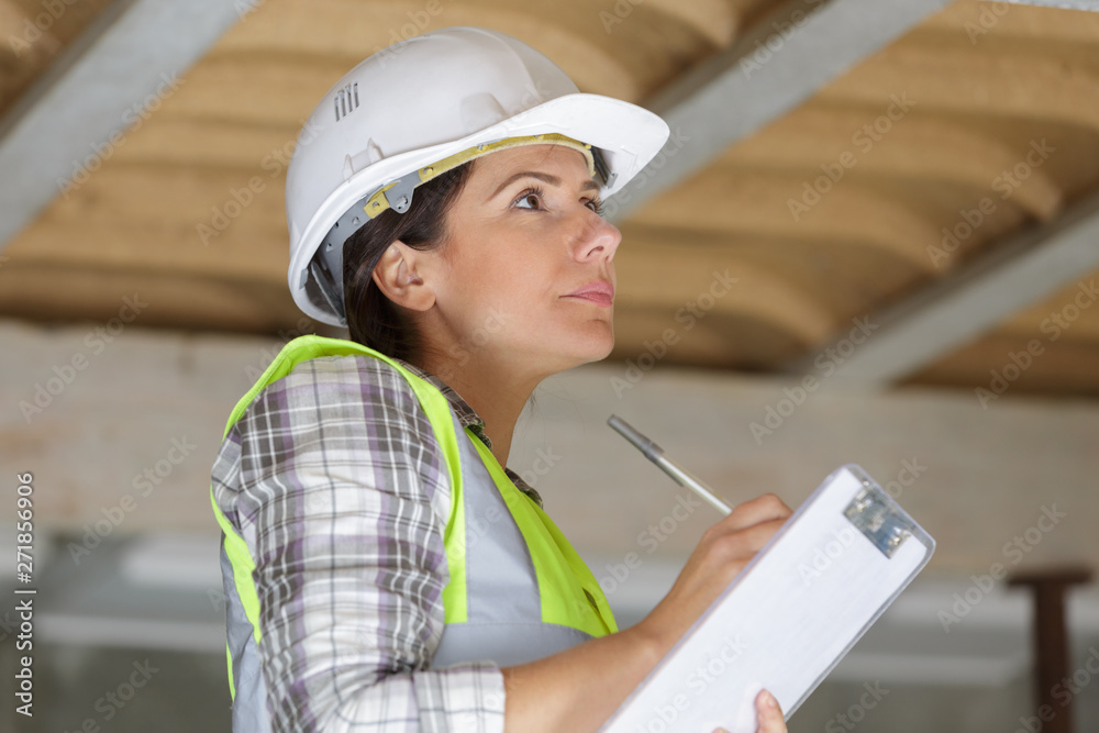 Fototapeta premium female builder in safety vest and hardhat writing in clipboard