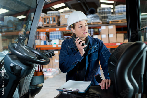 female engineer talking on walkie talkie next to forklift