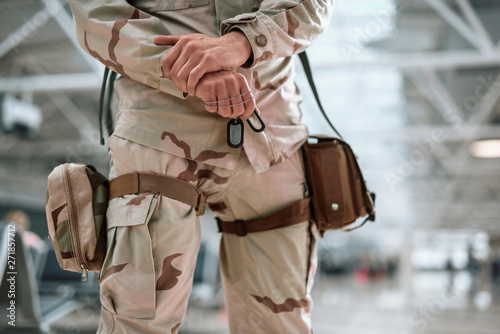 Cropped photo of American soldier in camouflage holding dog-tags in hand