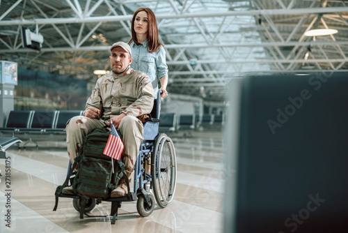 Wife carrying wheelchair and situating behind her husband in military uniform