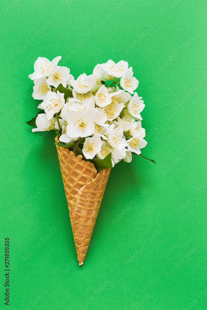Fototapeta Philadelphus or mock-orange flowers in a waffle ice cream cone on green background. Summer concept. Copy space, top view.