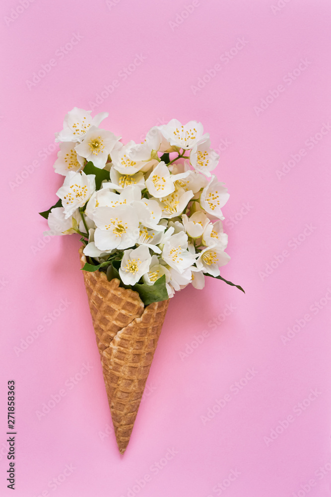 Fototapeta Philadelphus or mock-orange flowers in a waffle ice cream cone on pink background. Summer concept. Copy space, top view.
