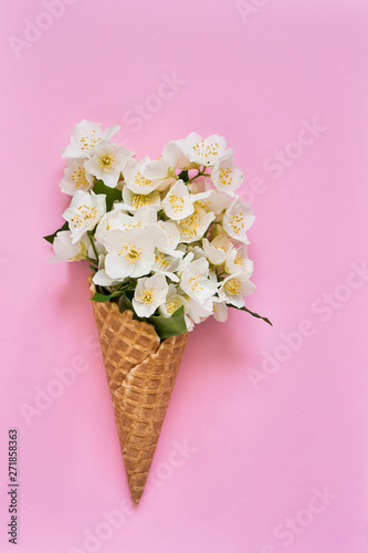 Philadelphus or mock-orange flowers in a waffle ice cream cone on pink background. Summer concept. Copy space, top view.