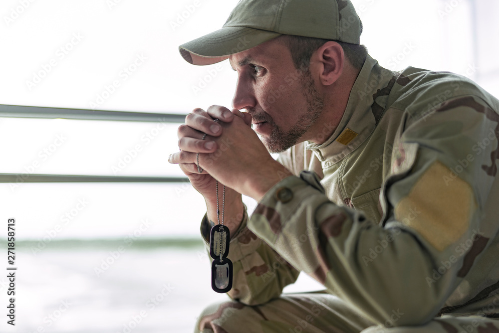 Low angle of American soldier in camouflage praying indoors Low angle of American soldier in camouflage praying indoors