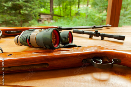 Binoculars laying on top of a rifle on a table photo