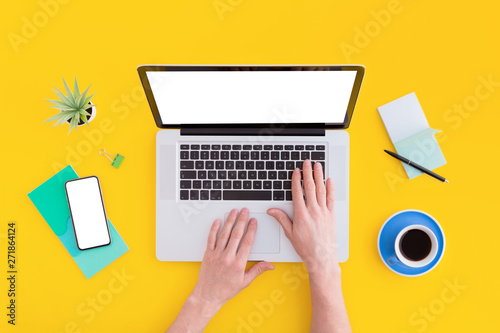 Hands on laptop keyboard. Top view on yellow workspace with stationery and macbook screen isolated.