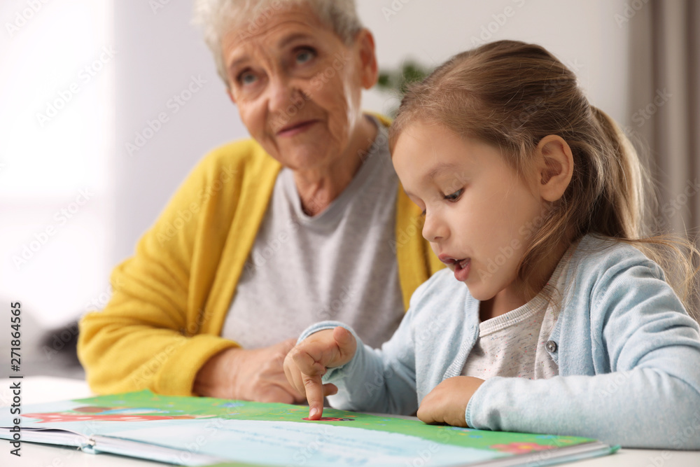 Cute girl and her grandmother reading book at home Cute girl and her grandmother reading book at home