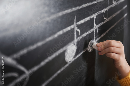 Child writing music notes on blackboard, closeup