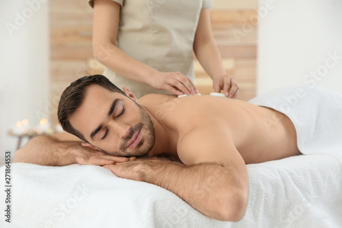 Handsome man receiving hot stone massage in spa salon