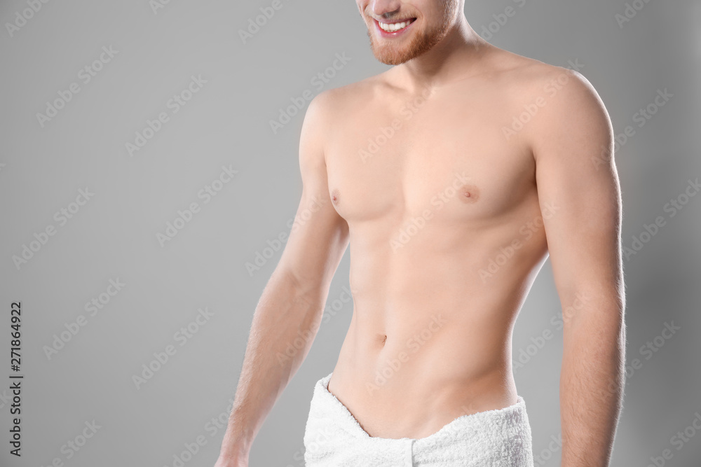 Fototapeta premium Young man with slim body in towel on grey background, closeup. Space for text