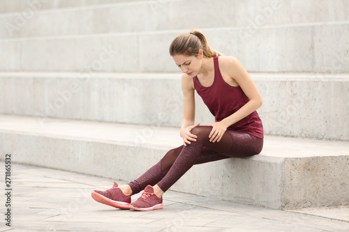 Woman in sportswear suffering from knee pain on stairs