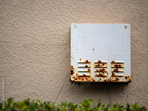 Rusty steel box with vents outside of home near bushes