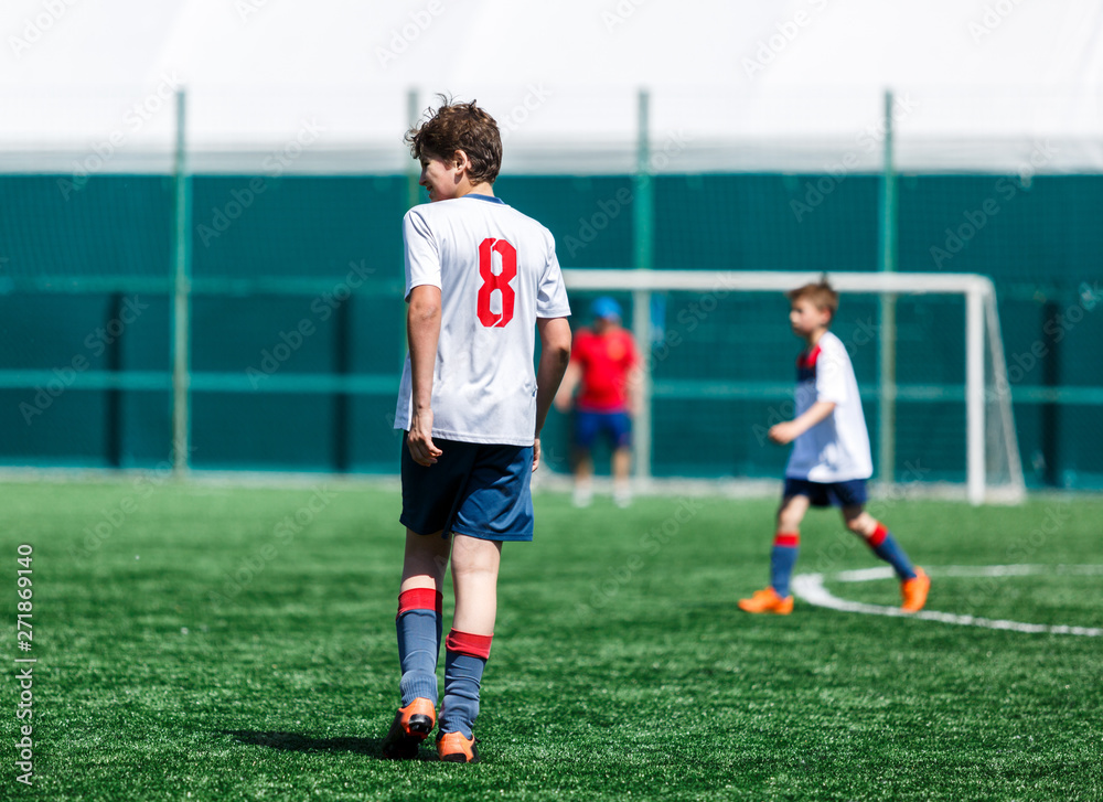 Boys in white  sportswear plays  football on field, dribbles ball. Young soccer players with ball on green grass. Training, football, active lifestyle for kids concept 