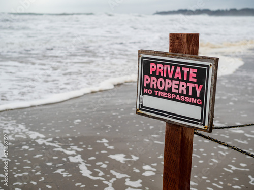 Private property no trespassing sign on pole and wire fence on beach property next to waves
