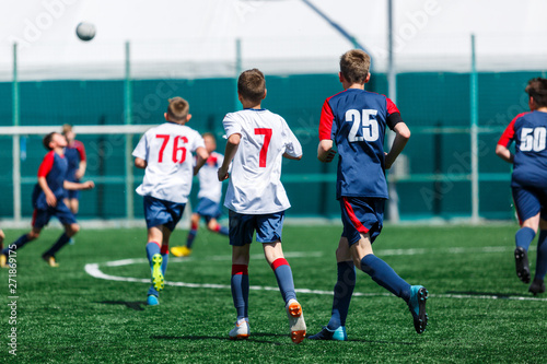 Boys in white and blue sportswear plays  football on field  dribbles ball. Young soccer players with ball on green grass. Training  football  active lifestyle for kids concept 