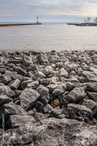 Rocky beach in foreground  harbor  pier and lighthouse in the back ground  moody sky