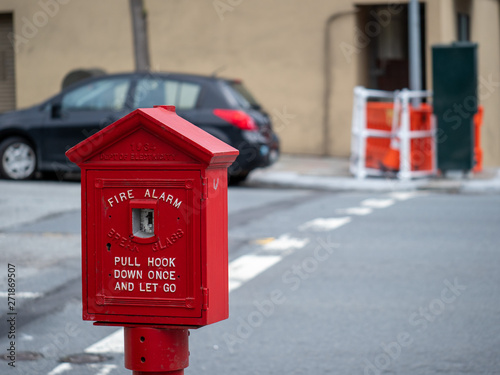 Weathered, old red fire alarm call box on street corner outside 