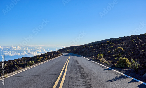 A road heading down from the Haleakala mountains with a view of clouds on the horizon.