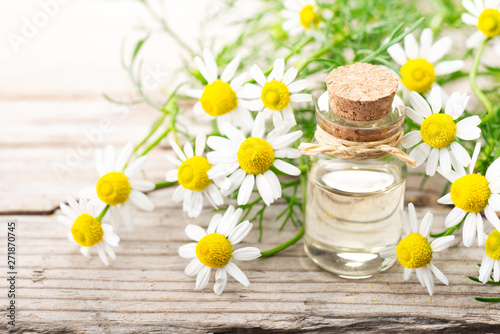 Chamomilla essential oil in the glass bottle, with fresh flowers, on the old wooden board