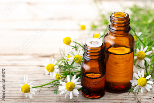 Chamomilla essential oil in the amber bottle, with fresh flowers, on the old wooden board