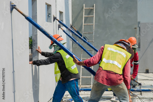 Construction worker are installing the precast concrete wall, orange safety helmet and green vest.