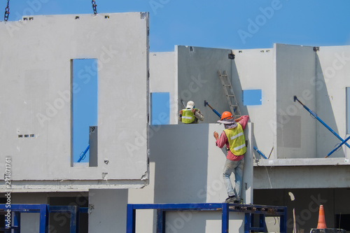 Construction workers are installing the precast concrete wall, orange safety helmet and green vest.