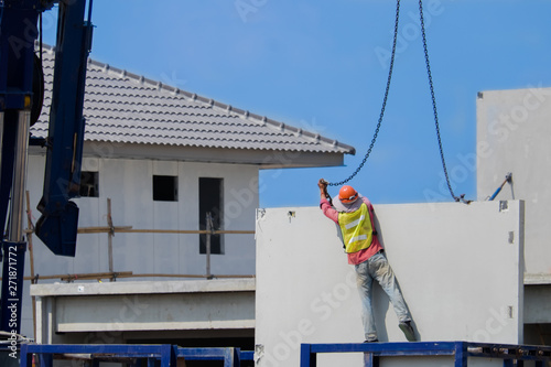 Construction worker are installing the precast concrete wall, orange safety helmet and green vest.